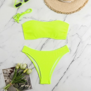 Flat lay of neon green bandeau bikini set with waffle texture and beach accessories