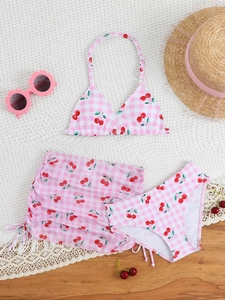 Flat lay of pink gingham cherry print three-piece girls bikini set with drawstring skirt