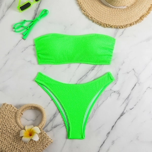 Flat lay of neon green textured bandeau bikini with sunglasses and vacation accessories