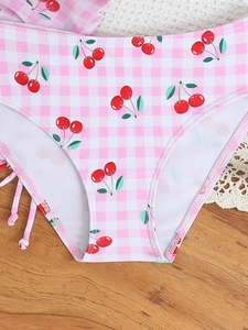 Detail of pink gingham bikini bottom with cherry print and side tie on lace background