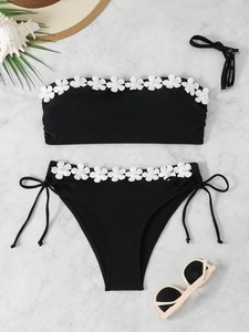 Detailed view of black bikini set with white floral embroidery and faux pearl accents