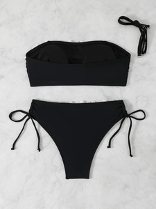 Detailed flat lay of black bandeau bikini set with white scalloped trim and side-tie bottoms