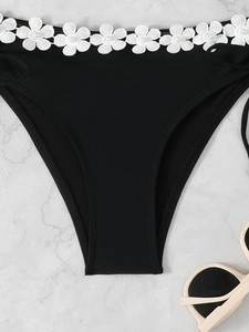 Close-up of black bikini bottoms with white floral lace embroidery and pearl accents