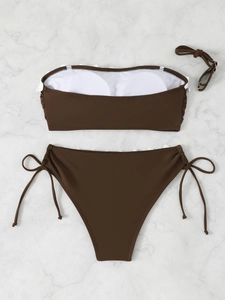 Flat lay of brown bikini with white embroidery and removable straps on marble surface