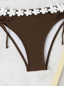 Detailed view of brown bikini bottoms featuring white floral embroidery and pearl accents