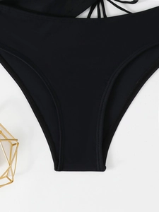 Detail of black bikini bottoms featuring side criss-cross strap design on a textured surface