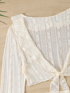 Close-up of white floral lace cardigan with tie-front detail and long sleeves on wood