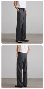 Macro detail of dark grey wide-leg trousers showing pleated texture and premium drape fabric
