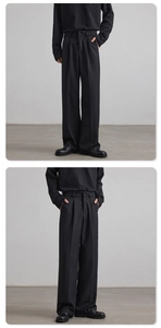 Detail view of black straight-leg trousers showing drape texture and pleat details