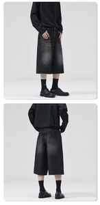 Detail view of baggy black denim shorts featuring heavy wash and raw whiskers finish