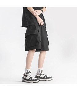 Detail of loose black cargo shorts featuring large 3D pockets and decorative webbing straps