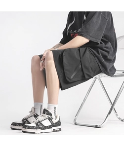Detail of black utility shorts with large pockets and branded monogram sneakers on white backdrop