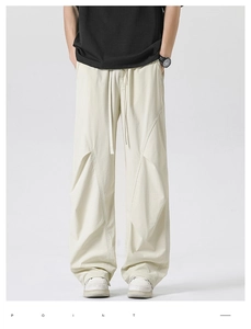 Detail of loose-fit white parachute pants with asymmetric patchwork stitching and drawstring