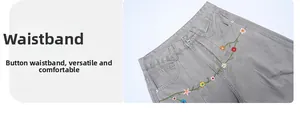 Detail of grey cotton pants waistband featuring colorful floral embroidery and metal button