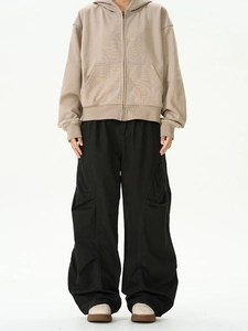 Styling-Detail der schwarzen Cargo-Hose und dem beigen Kapuzenpullover mit vielen Taschen