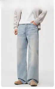 Men's light blue wide leg jeans paired with beige cardigan and brown shoes in a studio set