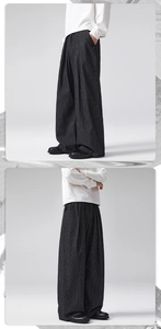 Detail of black pinstripe wide-leg trousers featuring triple pleats and a draped silhouette