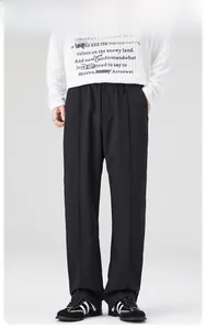 Détail du pantalon de costume noir à coupe droite avec plis marqués et tissu drapé