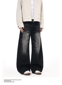 Detail of washed black oversized distressed denim jeans with ripped whiskers and loose fit