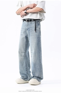 Détail d'un jean large bleu clair avec effet délavé et coutures au niveau des genoux