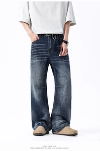 Dettaglio di jeans blu lavati a gamba larga con effetto baffi e catena in metallo