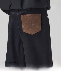 Detail of loose A-line jeans featuring dark blue denim with brown M-letter embroidered pocket