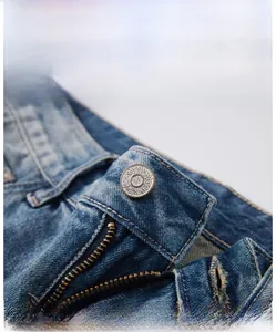 Detailansicht des geprägten Metallknopfs und Reißverschlusses an der hellen Jeanshose