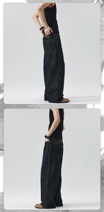 Detailed close-up of gold script embroidery on the back pocket of dark baggy denim pants