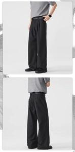 Detail view showing black pleated straight-leg trousers with elegant drape and slim belt