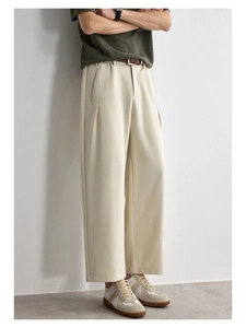 Detailed side view of beige pleated straight trousers with a smooth draping fabric texture