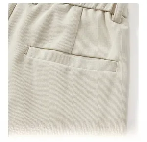 Detail view of beige textured corduroy trousers showing elastic waist and back pocket