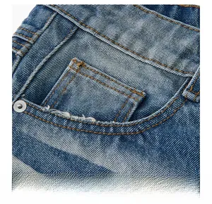 Detail of vintage blue washed denim front pocket with orange stitching and metal rivet