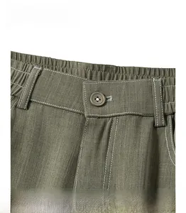 Dettaglio dell'elastico in vita con bottone e cuciture a contrasto sui pantaloni verdi