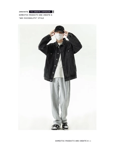 Full body view of loose fit black denim jacket styled with white tee and grey joggers