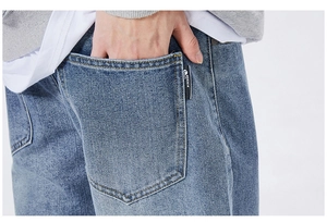 Detail of light blue washed denim jeans featuring orange stitching and black pocket tag