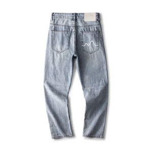 Détail du jean délavé bleu clair avec broderie vague blanche sur la poche arrière du pantalon
