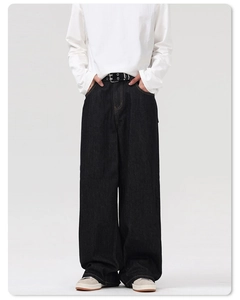 Detail of loose-fit dark grey denim jeans styled with a black grommet belt and grey sneakers