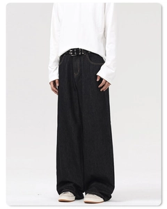 Detail of oversized dark black denim pants with textured fabric and double-hole leather belt
