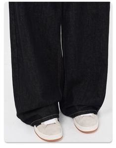 Detail of dark indigo denim fabric with yellow contrast stitching on loose wide-leg jeans