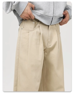 Close-up of khaki cotton twill trousers featuring double pleats and metallic rivets