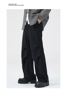 Detail view of avant-garde multi-layer knee pleats on black wide-leg trousers
