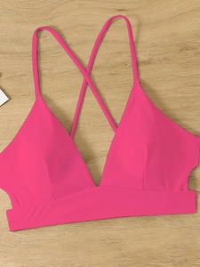 Pink sporty bikini top with criss-cross back straps and cutout details on wood background
