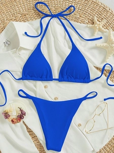 Flat lay of a ribbed bright blue halter bikini set with tie-side bottoms on a beach setup