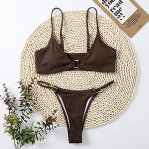 Detail of ribbed dark brown bikini with gold buckle accents on woven straw mat