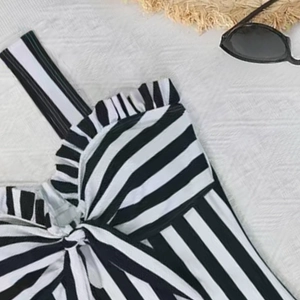 Detail of striped one-piece swimsuit with ruffle trim, bow knot, and summer beach accessories