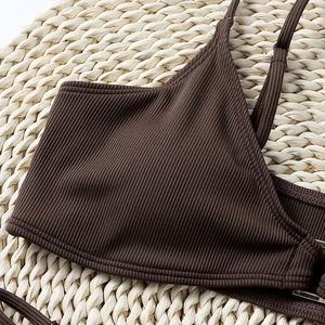 Close-up of brown ribbed fabric bikini top with fine shoulder straps on a straw mat
