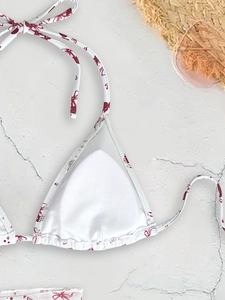 Three-piece bikini set featuring red bow print on white fabric with beach accessories
