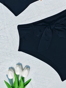 Detail of black high-waisted bikini bottom featuring a stylish side bow tie design