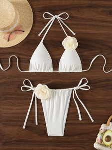 Dettaglio del top bikini a triangolo bianco con grande fiore 3D e lacci regolabili