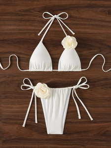 Set bikini bianco con fiori 3D e slip con laccetti su sfondo in legno scuro